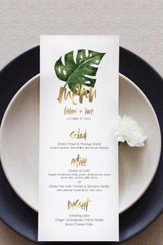 a menu card on a plate with a flower in the middle and gold foil lettering