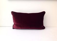 a red velvet pillow sitting on top of a white bed next to a framed photograph