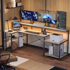 a computer desk with two monitors and a laptop on it in front of a wooden wall