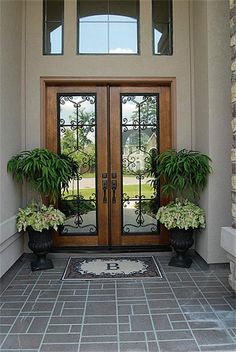 two potted plants sit on the front door of a house with glass doors and brick walkway