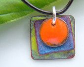 an orange and blue square pendant on a leather cord with a green leaf in the background