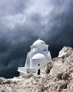 a white building sitting on top of a rocky hill under a cloudy sky with dark clouds