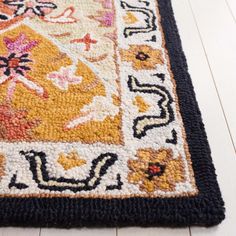 an area rug on the floor with white wood floors and black border around it that has colorful floral designs