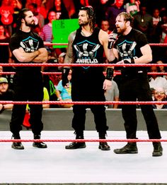 three men standing in the middle of a wrestling ring