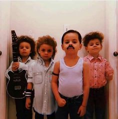 four children standing in front of a mirror with fake mustaches on their mouths and guitars behind them