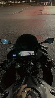 a person on a motorcycle driving down the street at night with their hand on the steering wheel