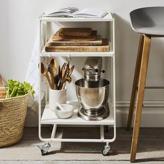 a kitchen cart with various items on it next to a chair and potted plant