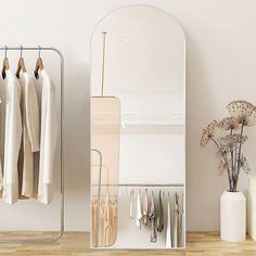 a white closet with clothes hanging on hooks and two vases filled with flowers next to it