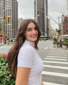 a woman standing in the middle of a street with tall buildings behind her and a traffic light above her head