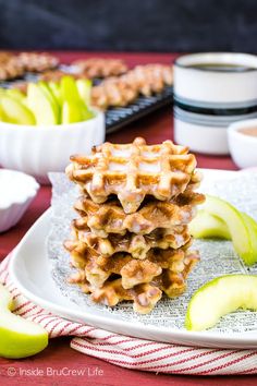 a stack of waffles sitting on top of a white plate next to sliced apples