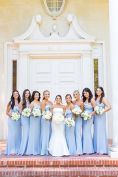 a group of women standing next to each other in front of a white door holding bouquets