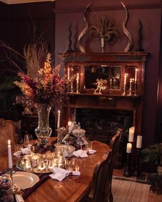 a dining room table is set with candles, plates and vases in front of the fireplace