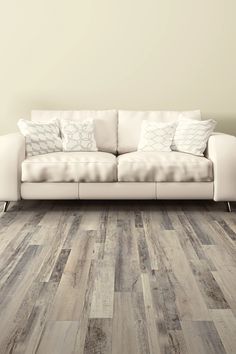 a white couch sitting on top of a wooden floor next to a wall with pillows