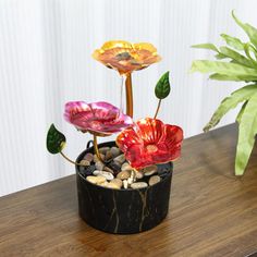 two fake flowers in a pot on a table next to a planter with rocks