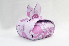 an origami rabbit shaped box with pink and white designs on the front, sitting on a white surface