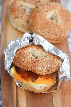 two bagels with cheese and bacon on them sitting on a cutting board next to each other