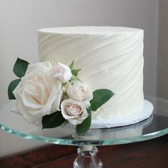 a close up of a cake on a glass platter with white frosting and flowers