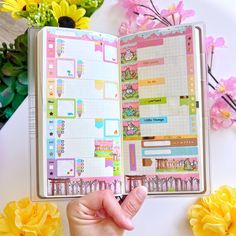 a hand holding an open planner book in front of flowers