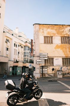 a man riding a motorcycle down the middle of a street next to tall white buildings