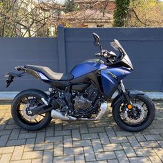 a blue motorcycle parked in front of a gray wall and brick floored driveway area