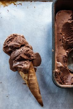 two scoops of chocolate ice cream next to each other on a metal tray with a spoon