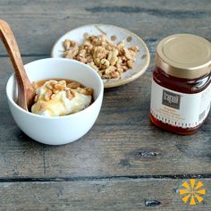 a bowl of food next to a jar of jam and spoon on a wooden table