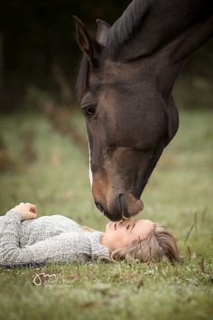 a woman laying on the ground next to a horse