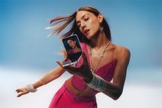 a woman in a pink dress holding up a cell phone with her face on the screen