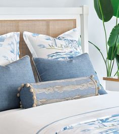 a bed with blue and white pillows on top of it next to a potted plant