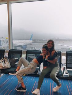 two women are posing for the camera in front of an airport terminal window with their arms around each other