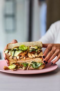 a woman holding a sandwich on top of a pink plate with lettuce and chicken