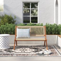 a wooden bench sitting on top of a rug in front of a white building with windows