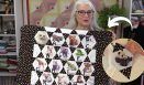 an older woman holding up a quilt with pictures on it and a panda bear hat