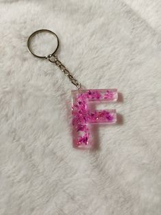 the letter f is made up of pink and purple glitters on a keychain