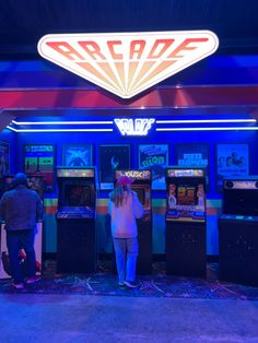 two people standing in front of arcade machines with neon signs on the wall behind them