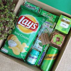 a box filled with lots of different types of snacks and drinks next to a potted plant