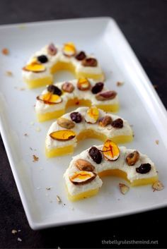 small pieces of food are arranged on a white plate with almonds and pistachio