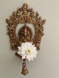 an ornate wooden clock with a flower in front of it on the wall next to a bell