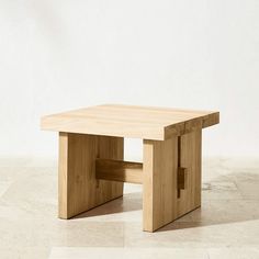 a square wooden table sitting on top of a tile floor next to a wall and white walls