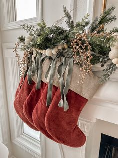 christmas stockings hanging from the fireplace mantel with greenery and berries on them in front of a window