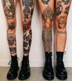 two legs with tattoos on them are standing next to each other in front of a wall