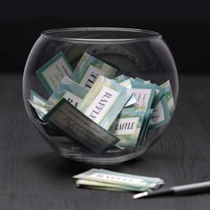 a glass bowl filled with money sitting on top of a table next to a pen