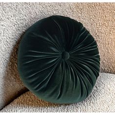 a green round pillow sitting on top of a white couch next to a beige wall