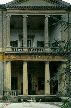 an old building with columns and steps leading up to the second floor, surrounded by greenery