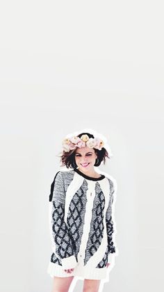 a woman with flowers in her hair standing next to a white wall and wearing a sweater