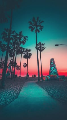 palm trees line the beach at sunset with people walking on the sand and in the distance