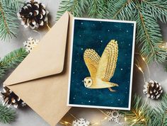 an owl is flying through the air near some pine cones and evergreen branches, with a card in front of it