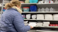 a woman is looking at dishes on shelves in a grocery store while holding a white frisbee