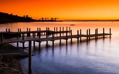 a long dock sitting in the middle of a body of water under a colorful sky