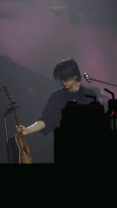 a woman standing in front of a microphone holding a guitar